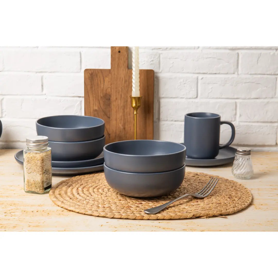 Set of matte gray ceramic stoneware bowls with rounded rims stacked neatly on a woven placemat from a 12-piece matte glaze dinnerware set for three.