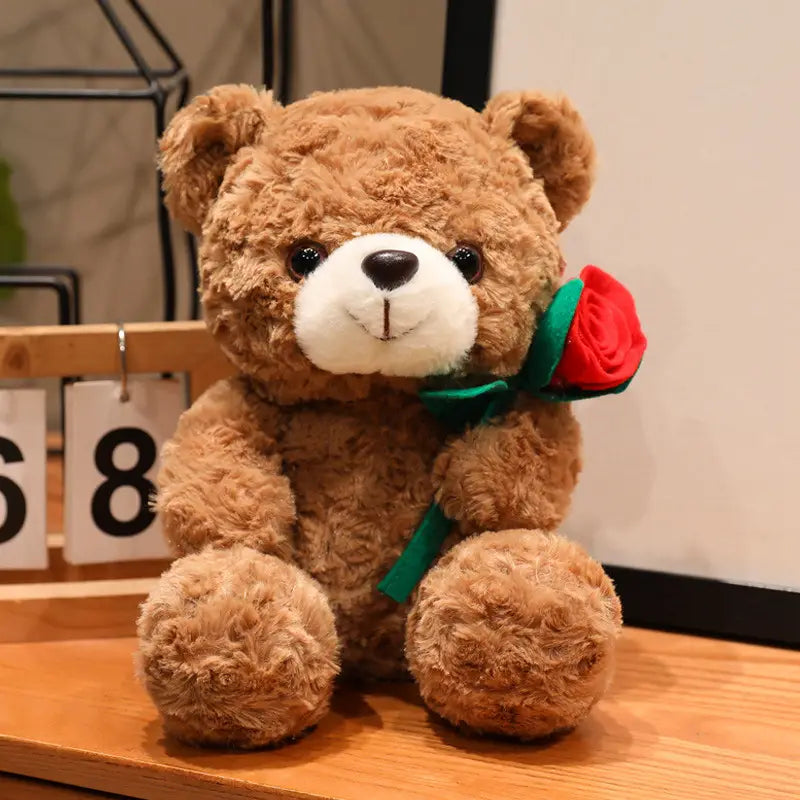 Ein brauner Plüsch-Teddybär mit weißer Schnauze und schwarzen Knopfaugen hält eine rote Rose mit grünem Band; präsentiert als Teddybär-Plüschtier mit Rosen, Valentinsgeschenk, 16–25 cm.