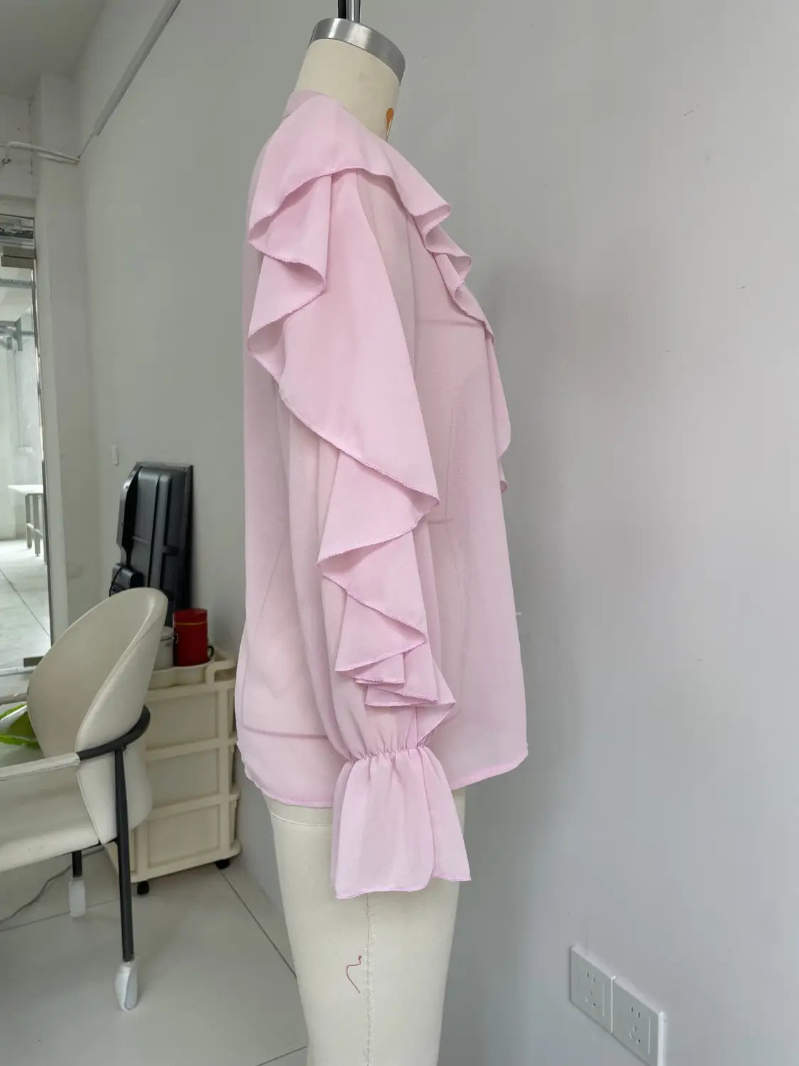 Eine weiche rosafarbene Volant-Chiffonbluse mit mehrlagigen Rüschen entlang der Ärmel und gerafften Bündchen, auf einem Schaufensterfigürchen präsentiert für das lässige Tragen mit langen Ärmeln.