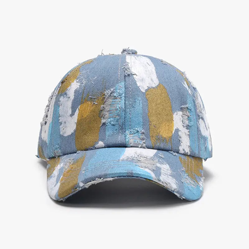 Une casquette de baseball en coton à projections de peinture vieillies, avec un motif de projections de peinture abstrait et vibrant dans des tons de bleu, de blanc et d’or.