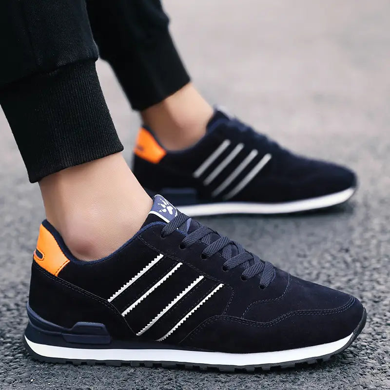Baskets de mode athlétiques en daim pour hommes en noir, avec des rayures blanches et des touches de couleur orange au talon, présentées depuis le côté arrière, du pointure 39 à 44
