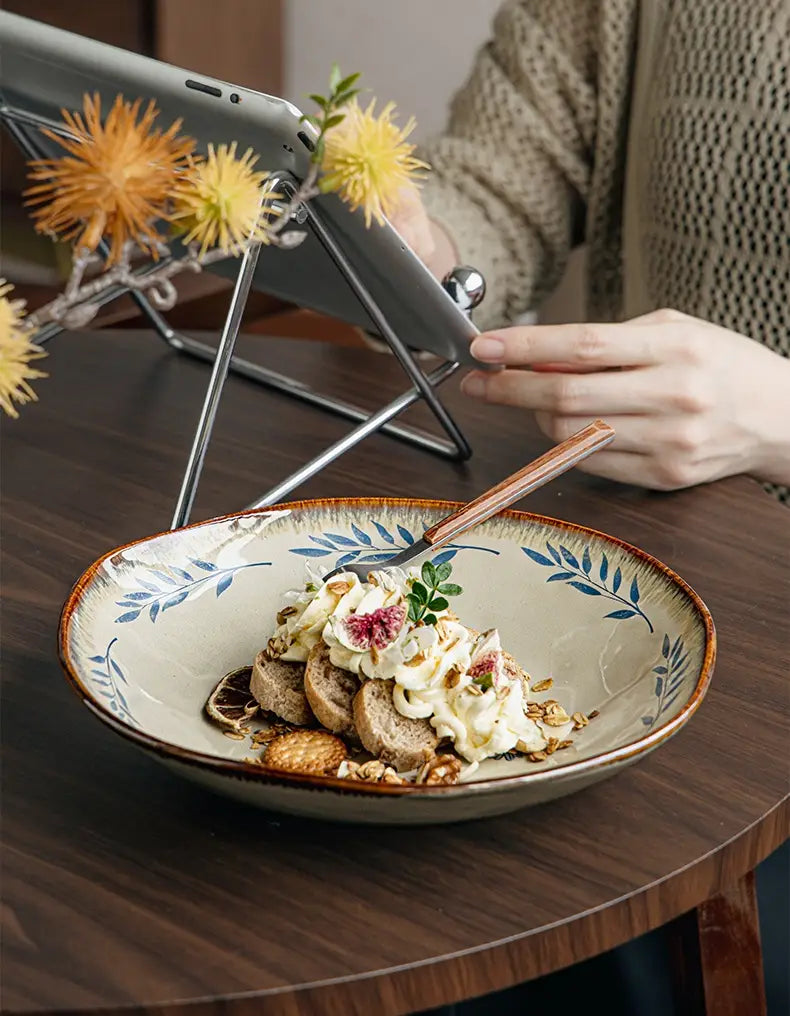 A 9-inch ceramic deep plate with a beige interior, blue leafy pattern, and brown rim holding a dessert topped with whipped cream.
