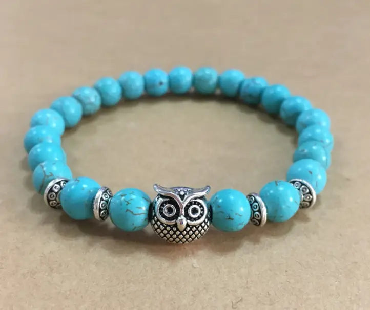 A turquoise beaded natural lapis lazuli and lava stone owl charm bracelet featuring a central silver owl charm and decorative metallic spacers.