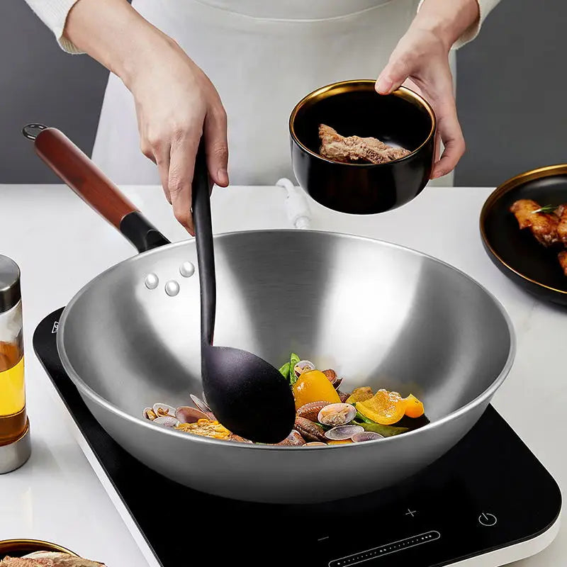 Glänzender Wok aus Edelstahl mit Schmiedeeisen-Antihaftbeschichtung, Holzgriff und schwarzer Silikon-Schöpfkelle zum Kochen.