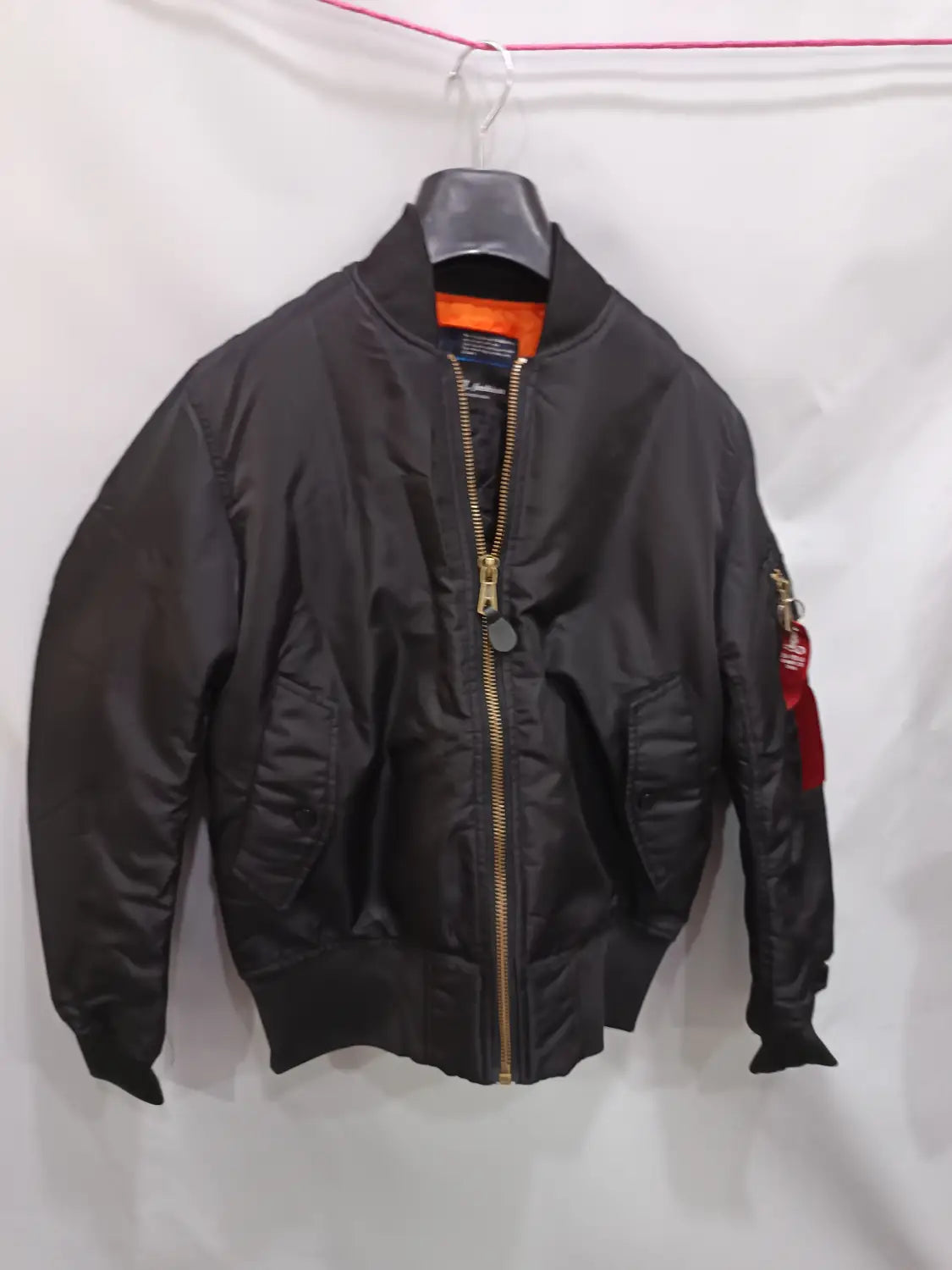 Men’s pilot cotton bomber jacket in black with orange lining and a red sleeve patch featuring gold zipper hardware.