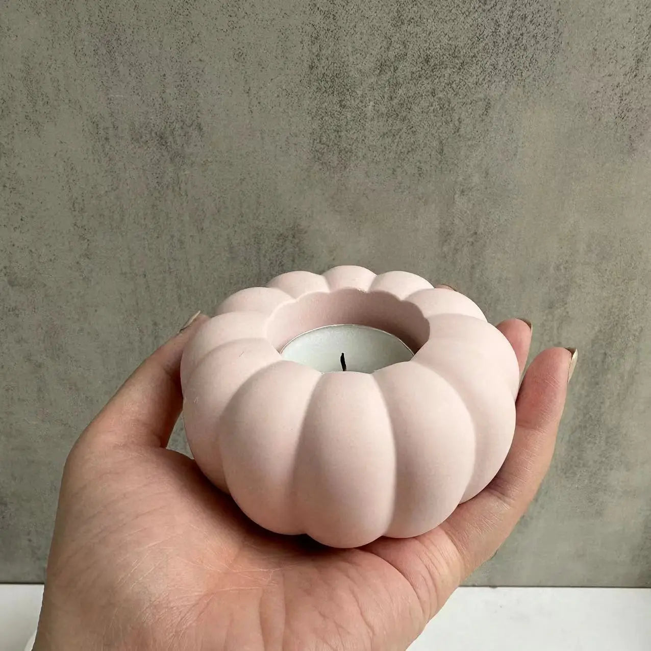 A soft pink ceramic pumpkin candle holder shaped by silicone mold t289, cradling a white tea light for decorative use.