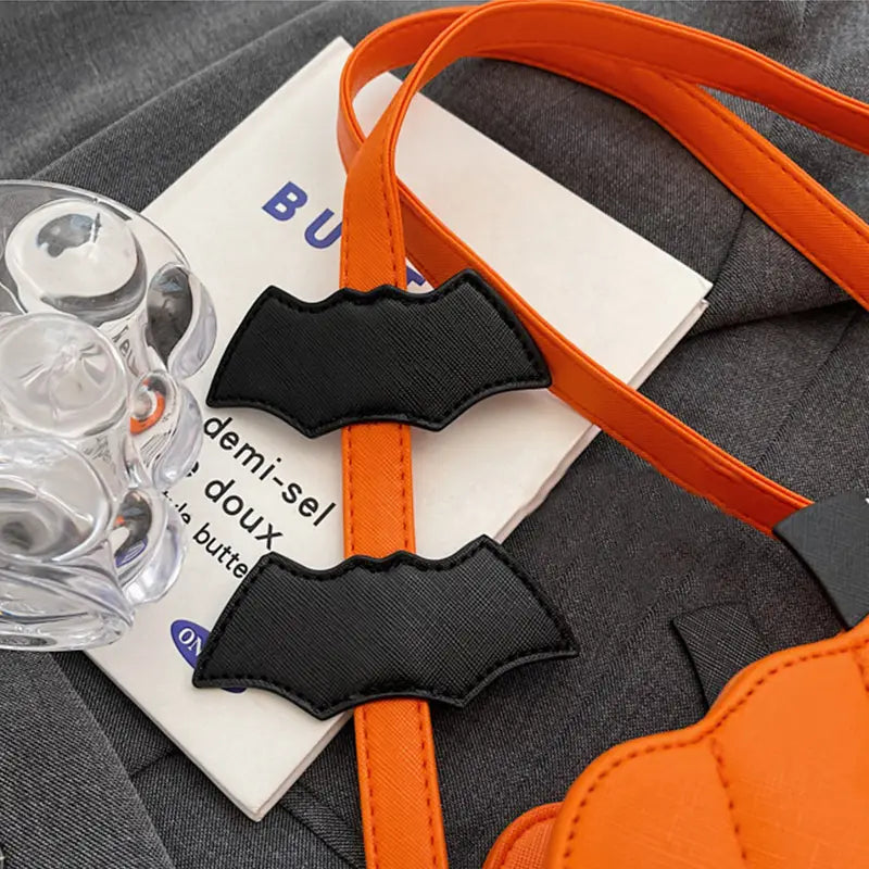 Orange strap with black bat-shaped charms attached to a funny pumpkin and bat crossbody bag with detachable charm.