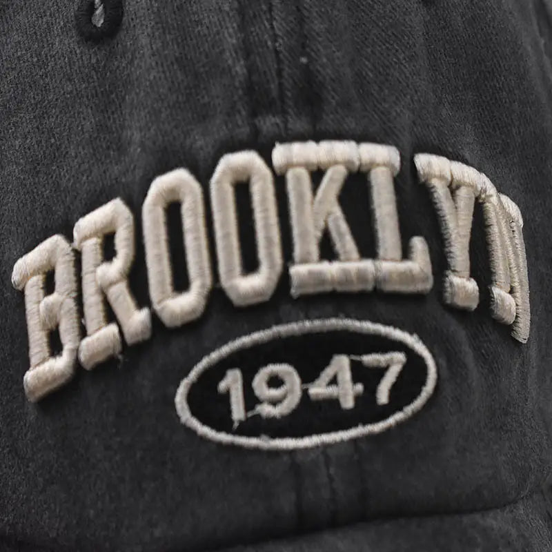 Black cotton baseball hat featuring embroidered brooklyn in cream-colored lettering and a matching oval patch with the number 1947.