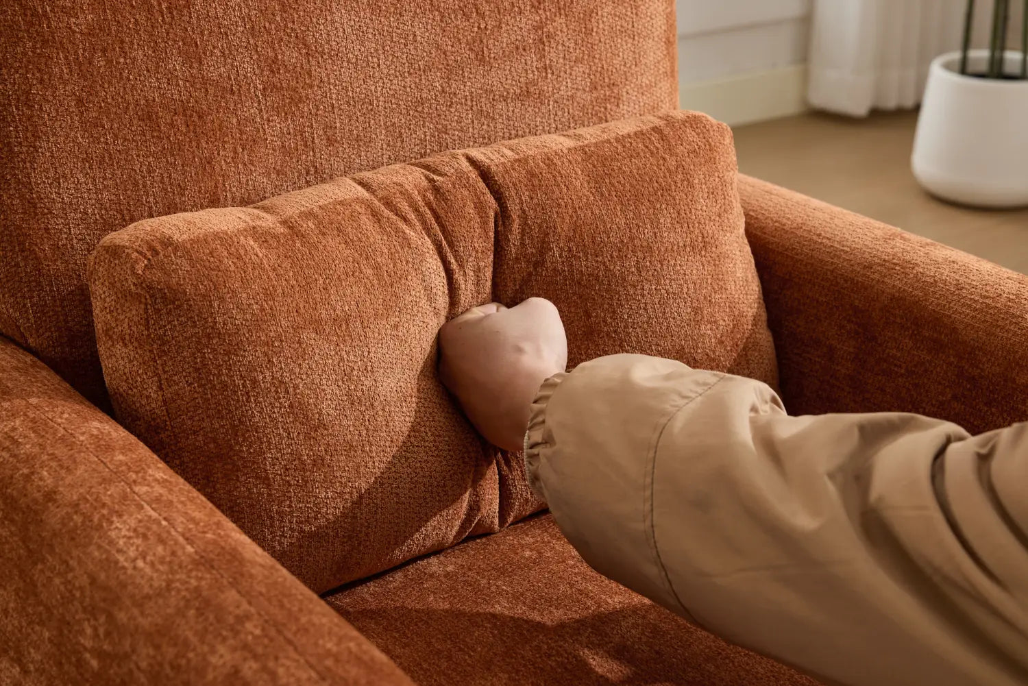 Ein moderner Bouclé-Akzent-Sessel, gepolstert mit rust-orangefarbenem Stoff, mit passendem, plüschig strukturiertem Kissen, eingebettet im Sessel.
