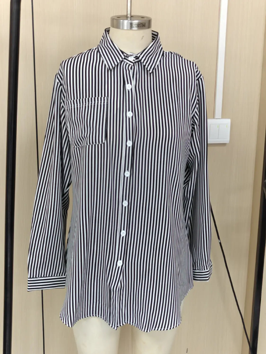 Chemise boutonnée à manches longues à rayures verticales noir et blanc, avec poche poitrine, conçue comme un haut décontracté.