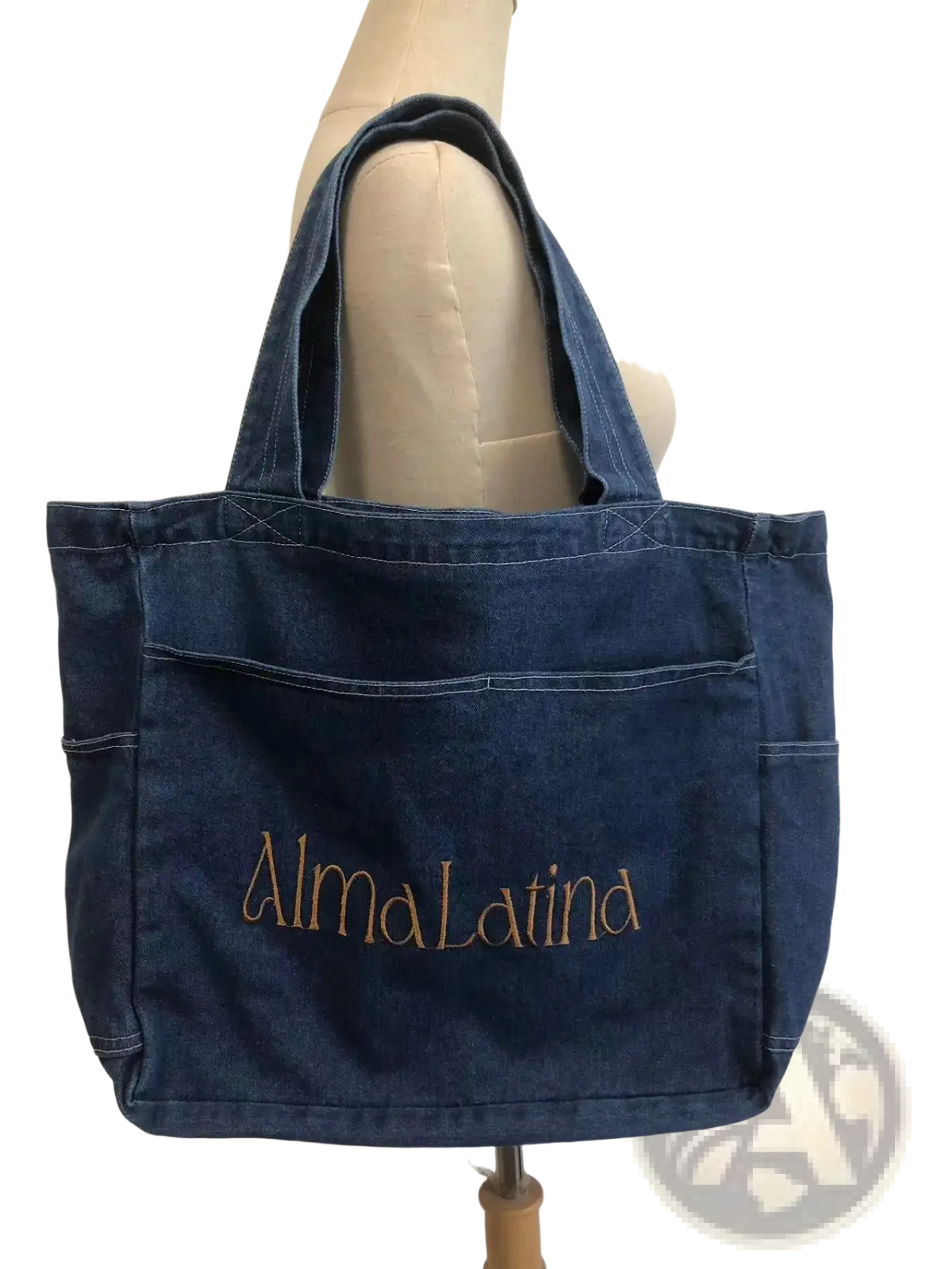 A dark blue denim tote bag with large capacity and gold embroidered alma latina text on the front