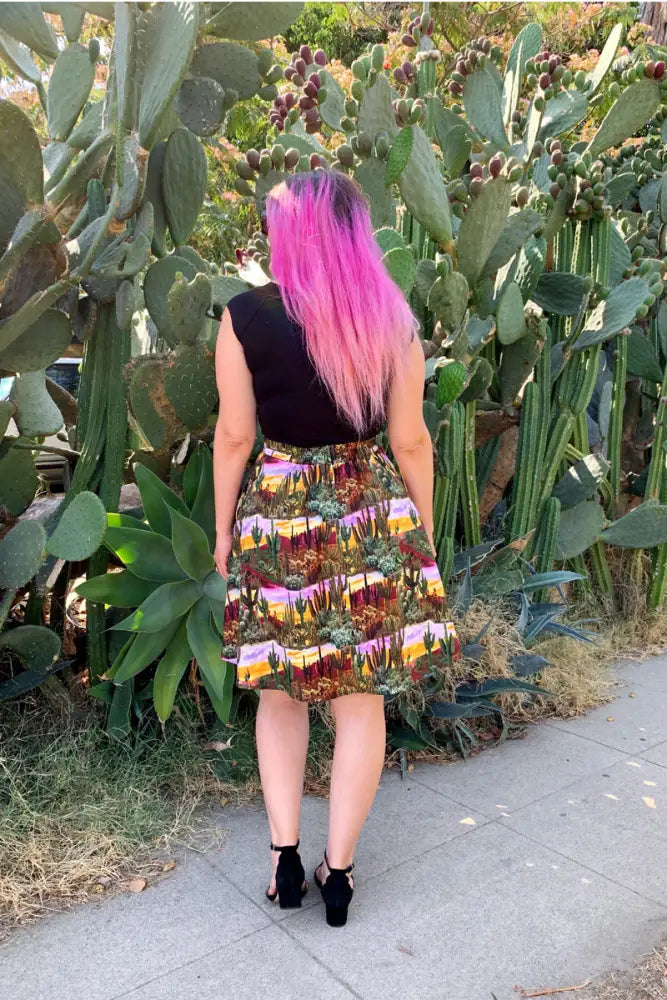 A vibrant a-line cotton skirt with a detailed desert cactus landscape print in warm pink yellow and brown hues