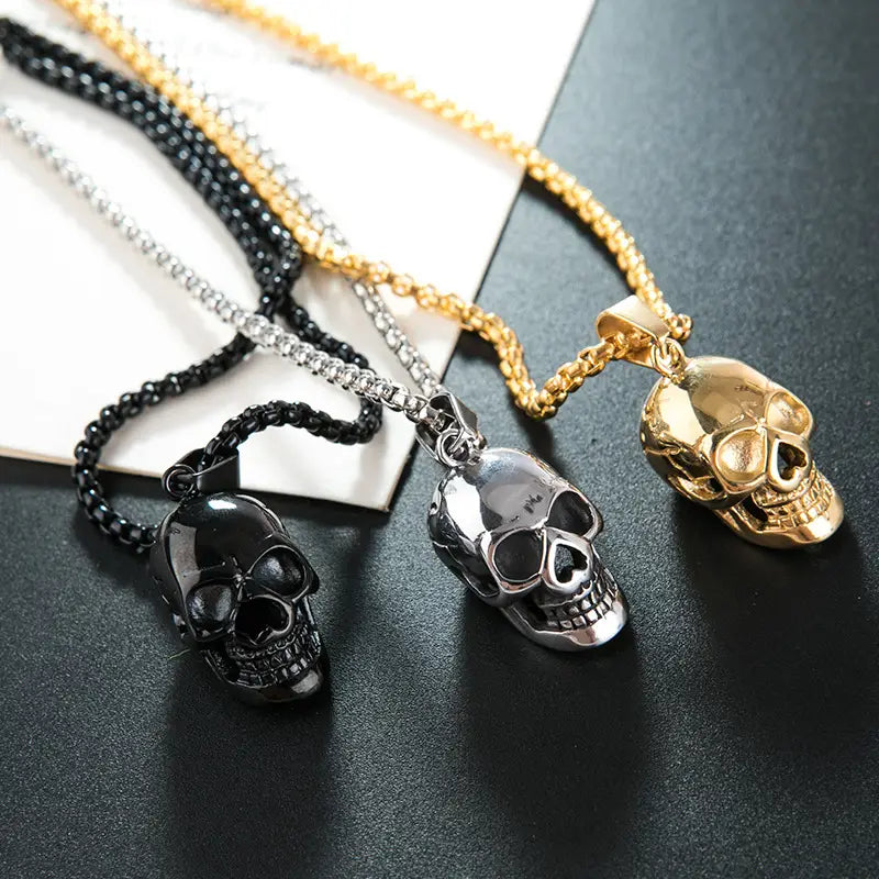 Three skull-shaped pendant necklaces in black silver and gold finishes made of titanium steel for men and women.