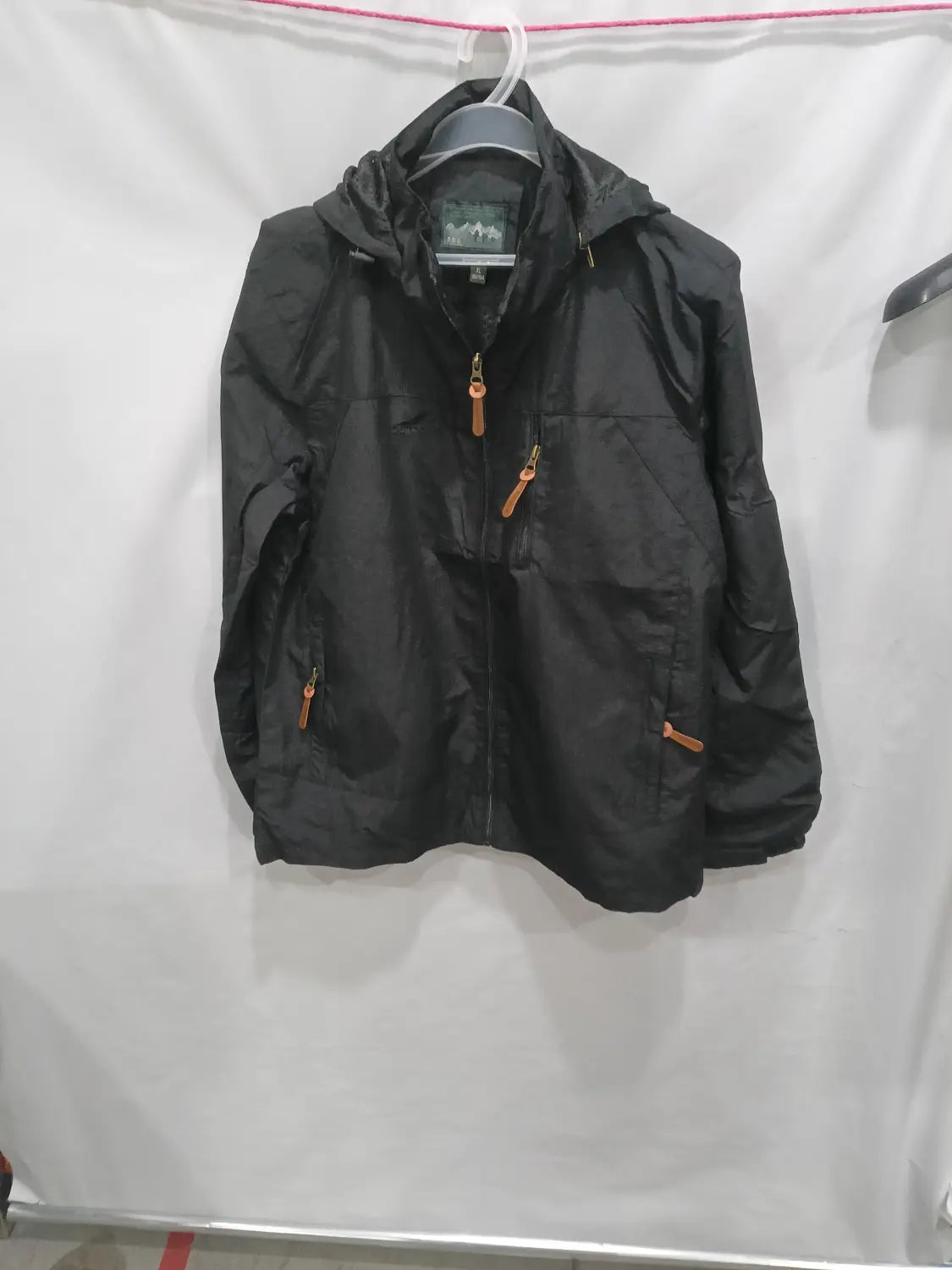 Chaqueta de senderismo con capucha impermeable color negro, con tiradores de cremallera color camel y una etiqueta de marca sutil en el cuello.