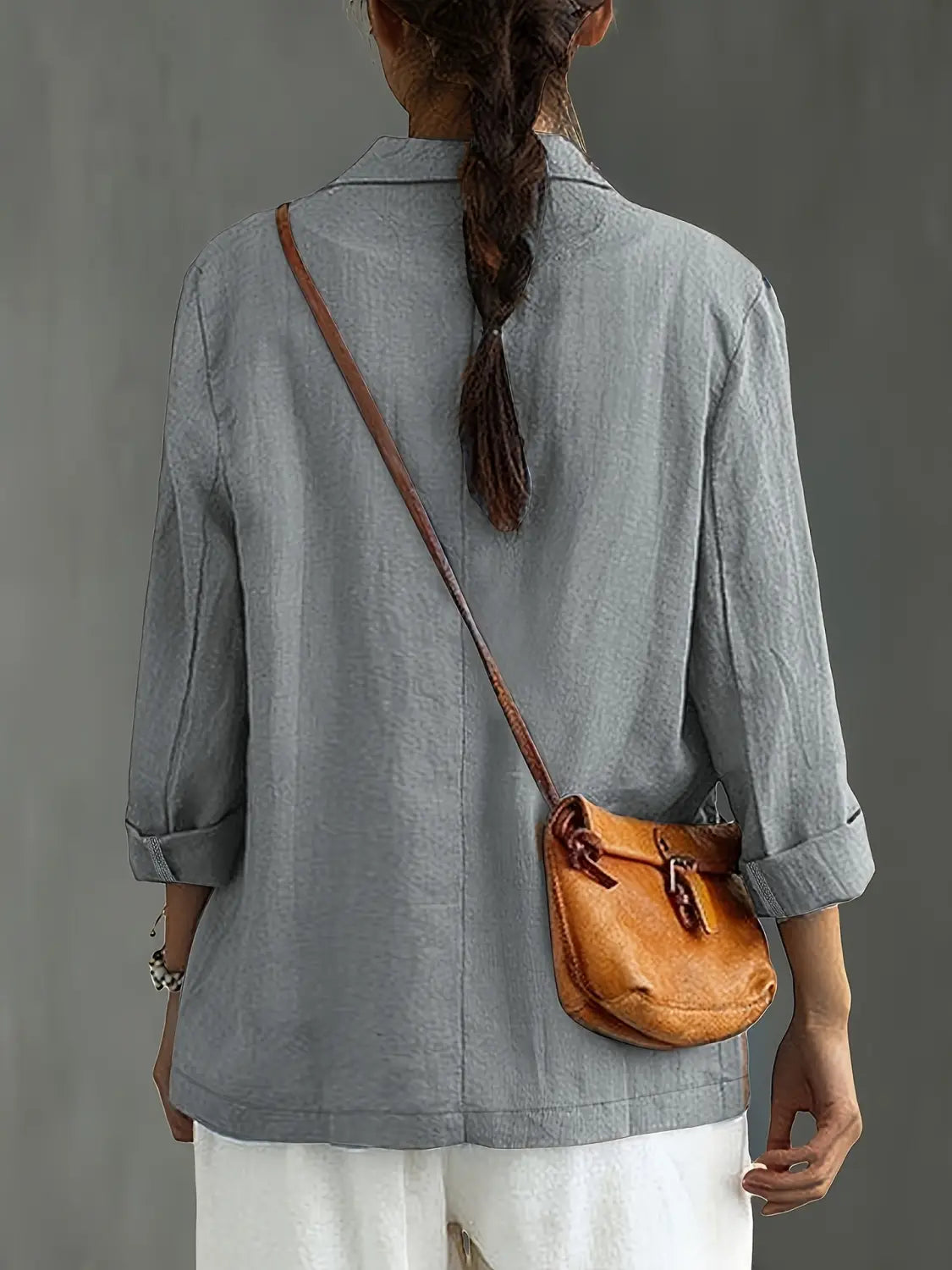 un bolso cruzado de cuero color camel con cierre de cordón y correa marrón, complementando un blazer de lino para mujer, casual y de trabajo.