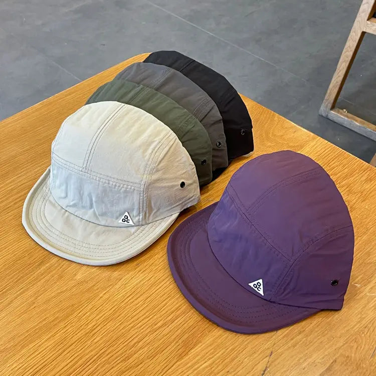 Quick drying short brim five panel cap in maroon with purple and beige panels made of lightweight fabric featuring a subtle triangular logo on the front.