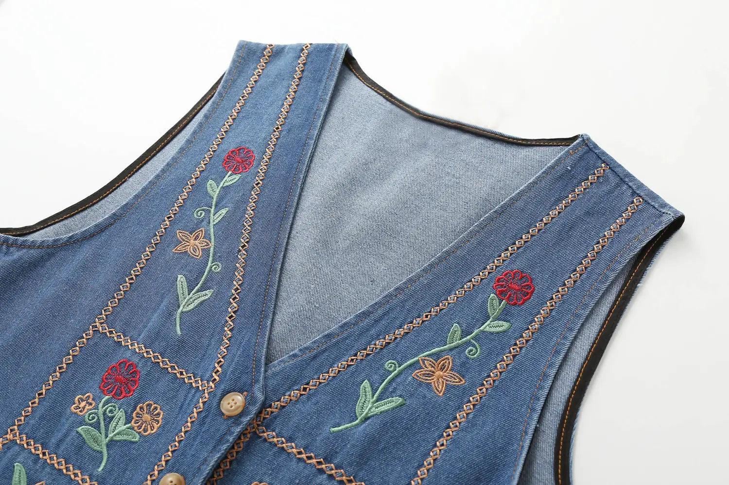Jeansweste mit farbenfroher roter, orangefarbener und grüner floraler Stickerei auf mittelblauem Stoff, betitelt bestickte florale Jeansweste.