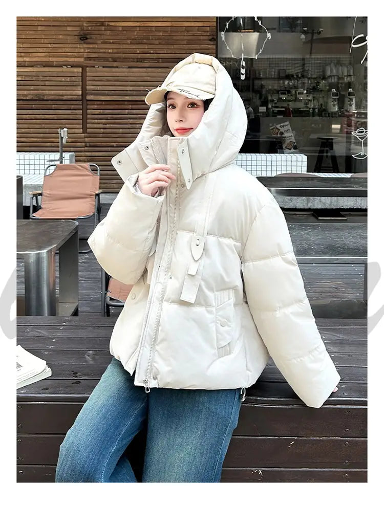 Veste courte matelassée à capuche pour femme couleur crème, avec panneaux matelassés, fermeture éclair frontale et deux poches latérales, conçue pour l’habillement d’hiver chaud.