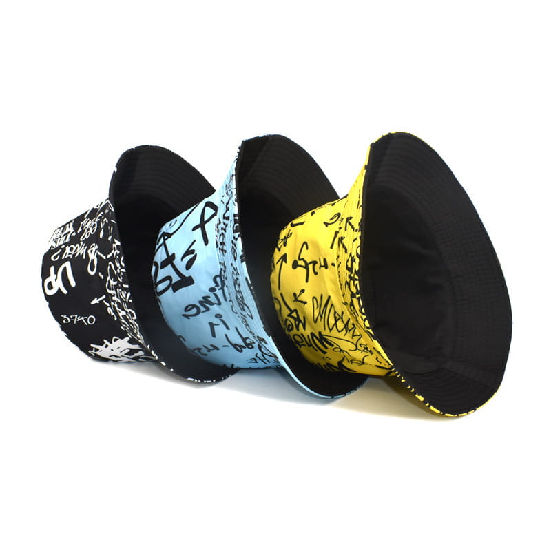 Trois chapeaux bob style graffiti en noir, bleu clair et jaune, avec un lettrage audacieux sur une surface en tissu respirant, conçus comme des chapeaux de voyage avec protection solaire.