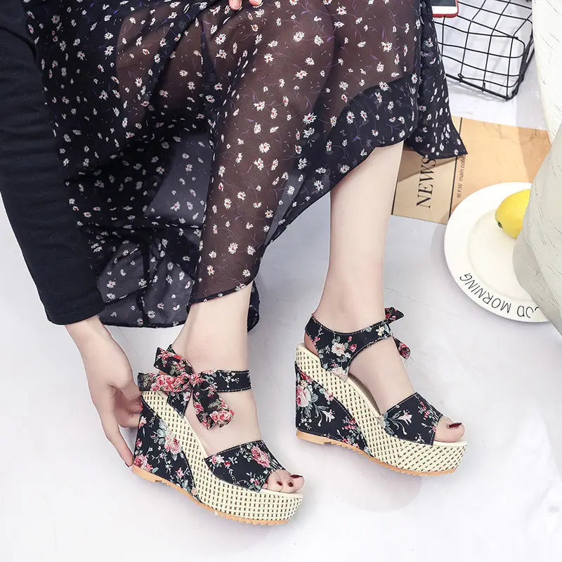 Black floral bohemian platform wedge sandals with a woven beige platform and decorative bow ankle ties.
