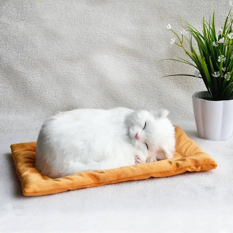A fluffy white realistic breathing plush cat figurine curled up and sleeping peacefully on a soft orange plush pet bed.