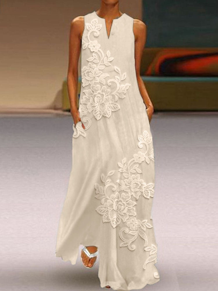 Une robe longue sans manches ivoire pâle, élégante, présentant une dentelle florale appliquée blanche et des détails floraux complexes le long de l’avant et des côtés.