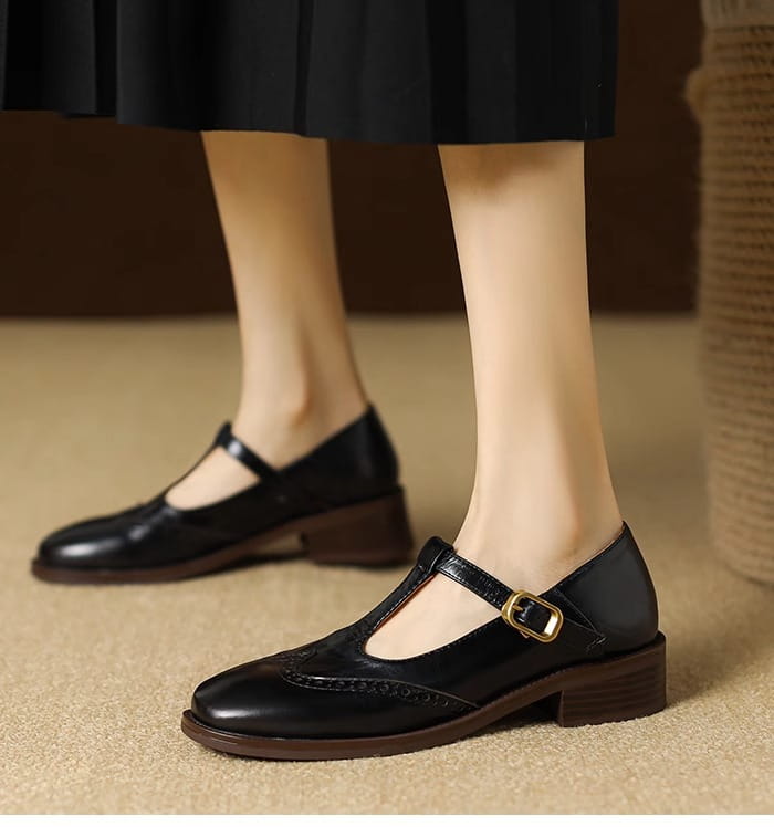 Schwarze Leder-Brogue-Mary-Jane-Pumps mit klobigem Absatz mit goldfarbenem Schnallenverschluss und detaillierter Brogue-Verzierung am Vorderteil.