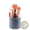 A cylindrical makeup brush holder encrusted with blue pink and silver rhinestones featuring a clear handle and coral grip