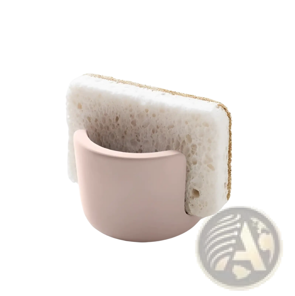 A soft pink ceramic Diatom Mud sponge rack holding a white textured cleaning sponge with a golden-brown abrasive edge