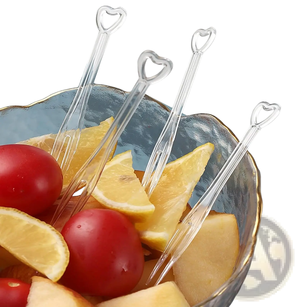 Four transparent disposable silver heart fruit picks made of plastic arranged in a bowl with sliced citrus and tomatoes
