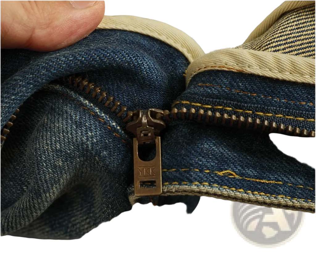 Bronze metal zipper pull engraved with mk on dark blue denim in distressed patchwork denim jeans for men