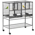 Black metal divided breeder bird cage with two compartments housing a green and yellow parakeet on perches