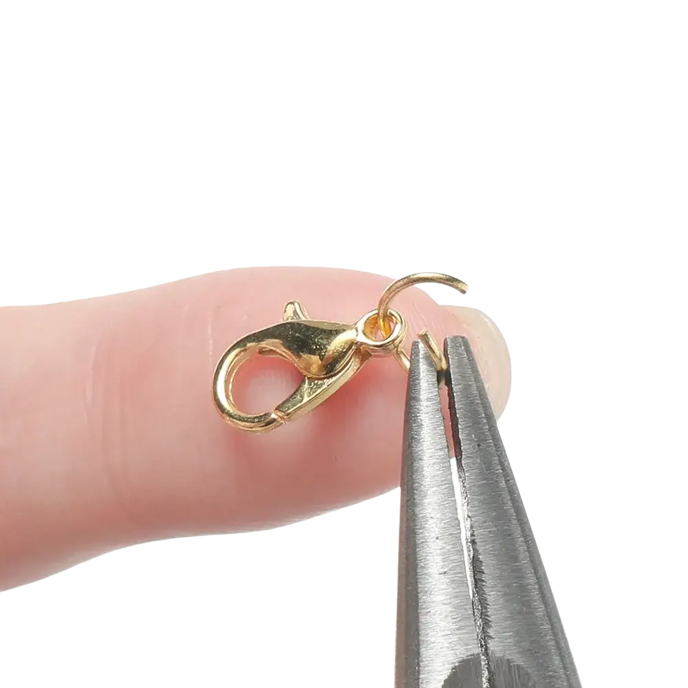 Gold-toned lobster clasp with small loop held by pliers in diy jewelry making findings kit with tools