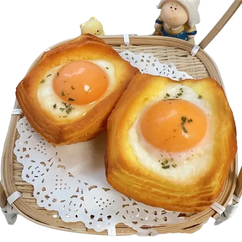 Dog bread slow rising squishy toy resembling golden brown egg-in-pastry baked goods with runny yolks and green herb garnish