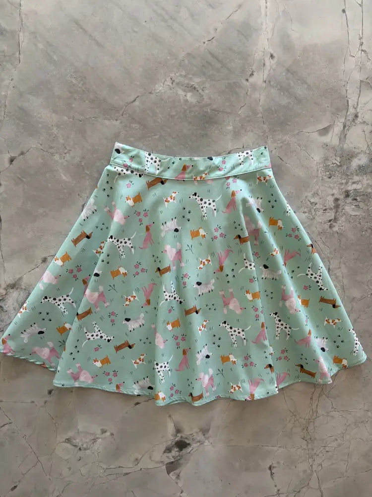 A pastel mint cotton skater skirt with a flared silhouette featuring dog breeds and floral accents in pink brown and white