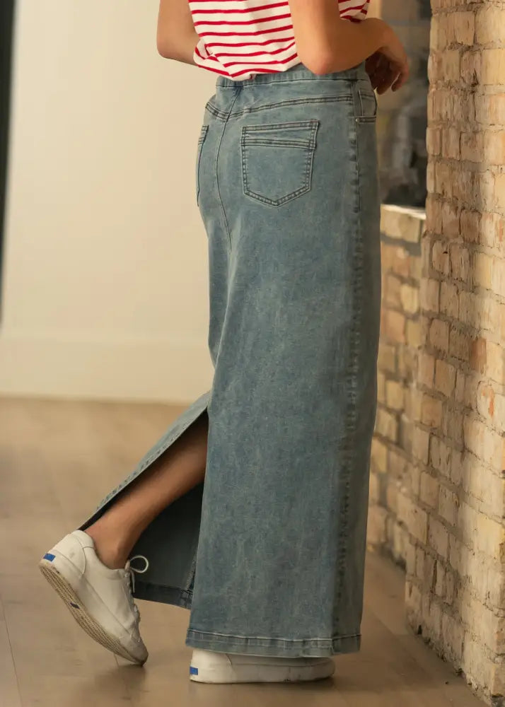 Light-wash stretch denim maxi skirt with side slit and classic back pocket design shown from the back side