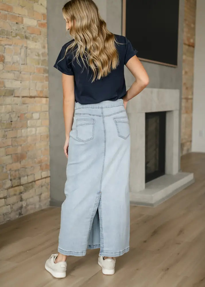 Donna light wash stretch denim maxi skirt with front slit and back pockets shown from the back side