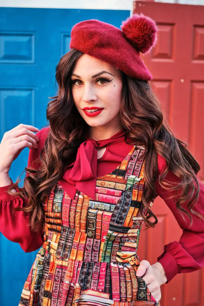 A plush red beret with a fuzzy pom-pom paired with a cotton fit and flare bookshelf print dress with pockets