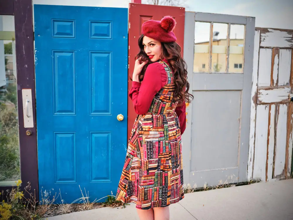 A woman wearing a bookshelf print cotton fit and flare dress with pockets and a red long-sleeved top and beret