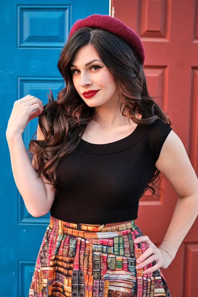 A woman wears a burgundy plush beret paired with a vintage book print cotton a-line skirt with pockets