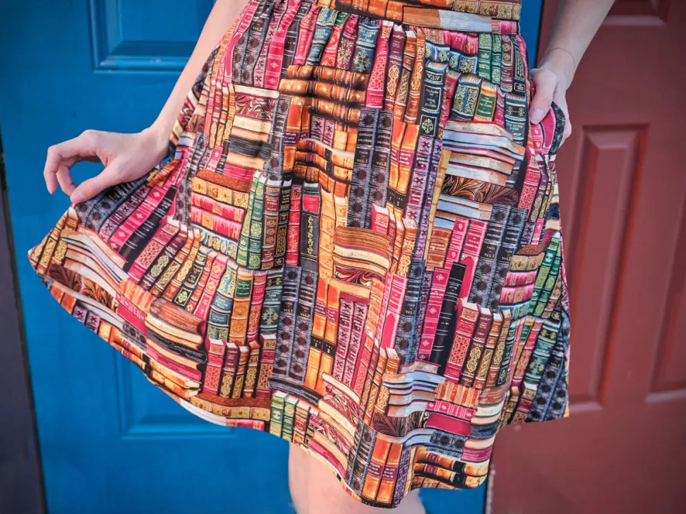A vibrant cotton a-line skirt with pockets featuring a colorful vintage book spine print in reds oranges greens and browns