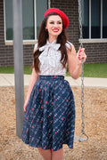 A woman wears a Doris navy pleated heartbreaker skirt with red hearts and white barbed wire patterns paired with a white blouse