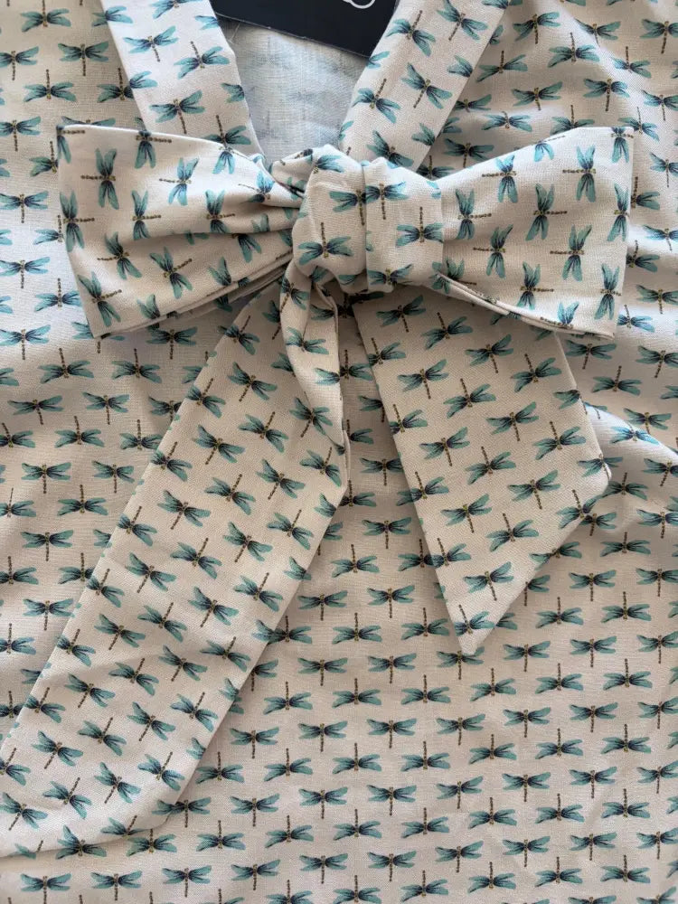 A cream-colored cotton retro dragonfly blouse with teal wing patterns and a matching bow at the neckline