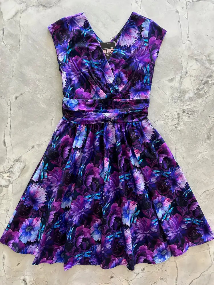 A vibrant purple and blue cotton Dragonfly Floral Greta v-neck dress with a fitted waistband and flared skirt