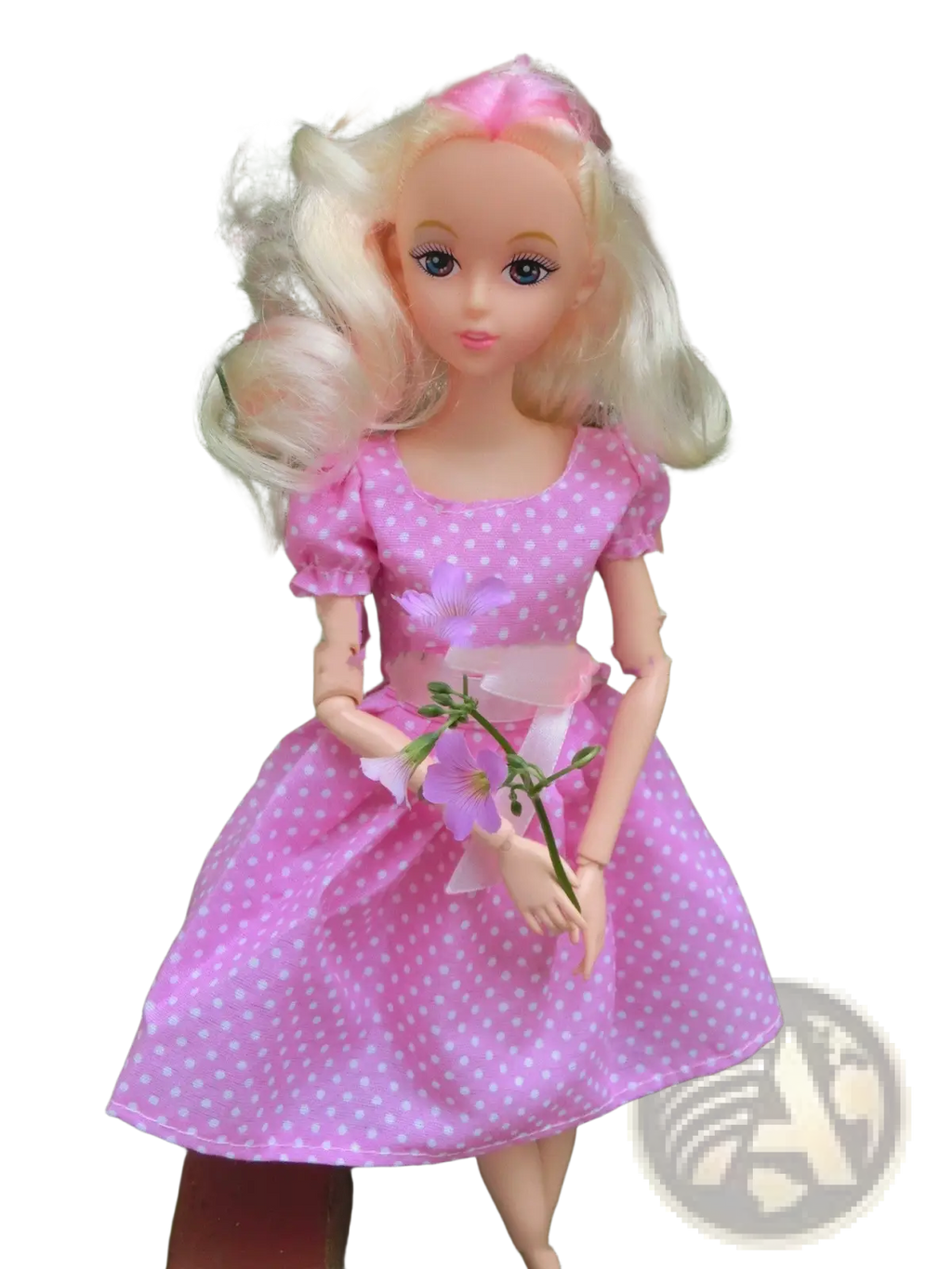 A blonde-haired dress up doll wearing a pink polka dot fashion suit holding purple flowers for kids