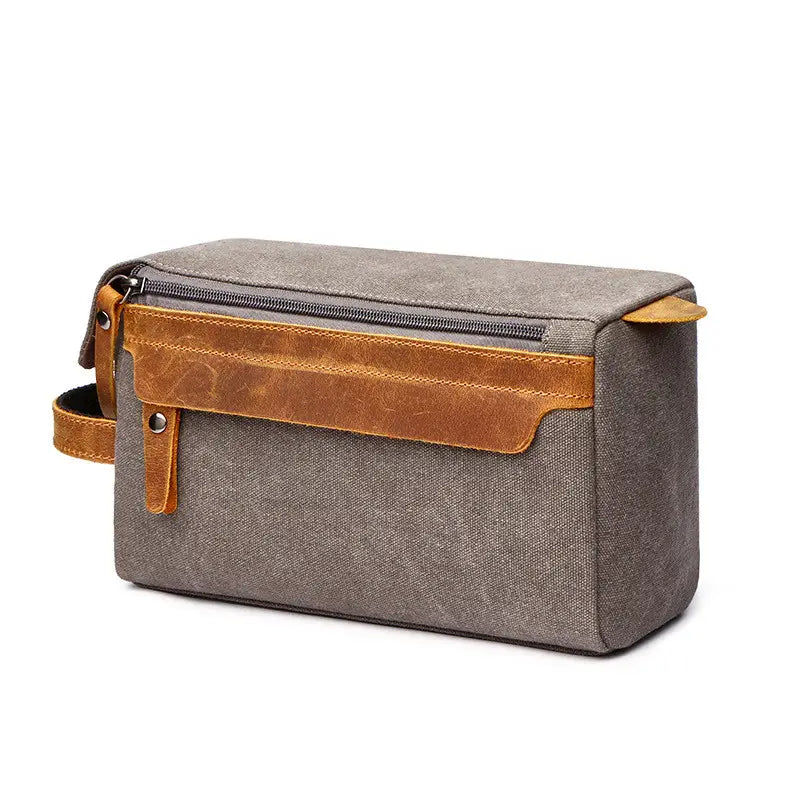 Gray canvas toiletry bag with tan leather accents and zipper closure designed as a large portable travel storage case.