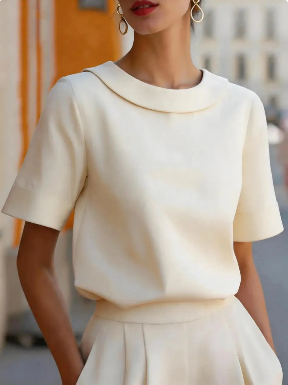 Cream-colored women solid color short sleeve versatile top with rounded collar and soft structured fabric.