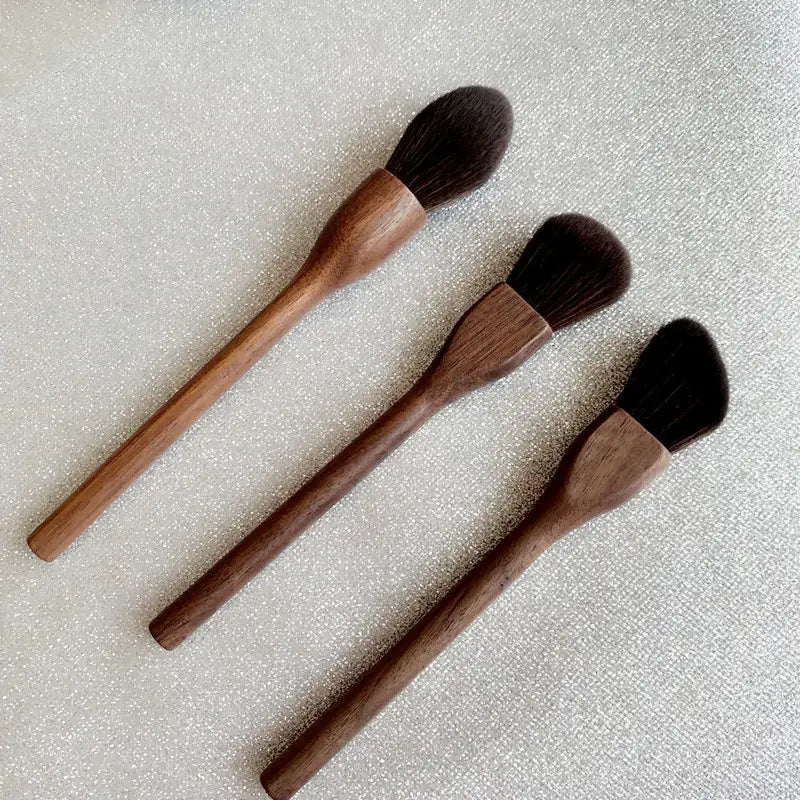 Set of three walnut wood makeup brushes with dark brown soft fiber bristles and tapered ergonomic wooden handles.