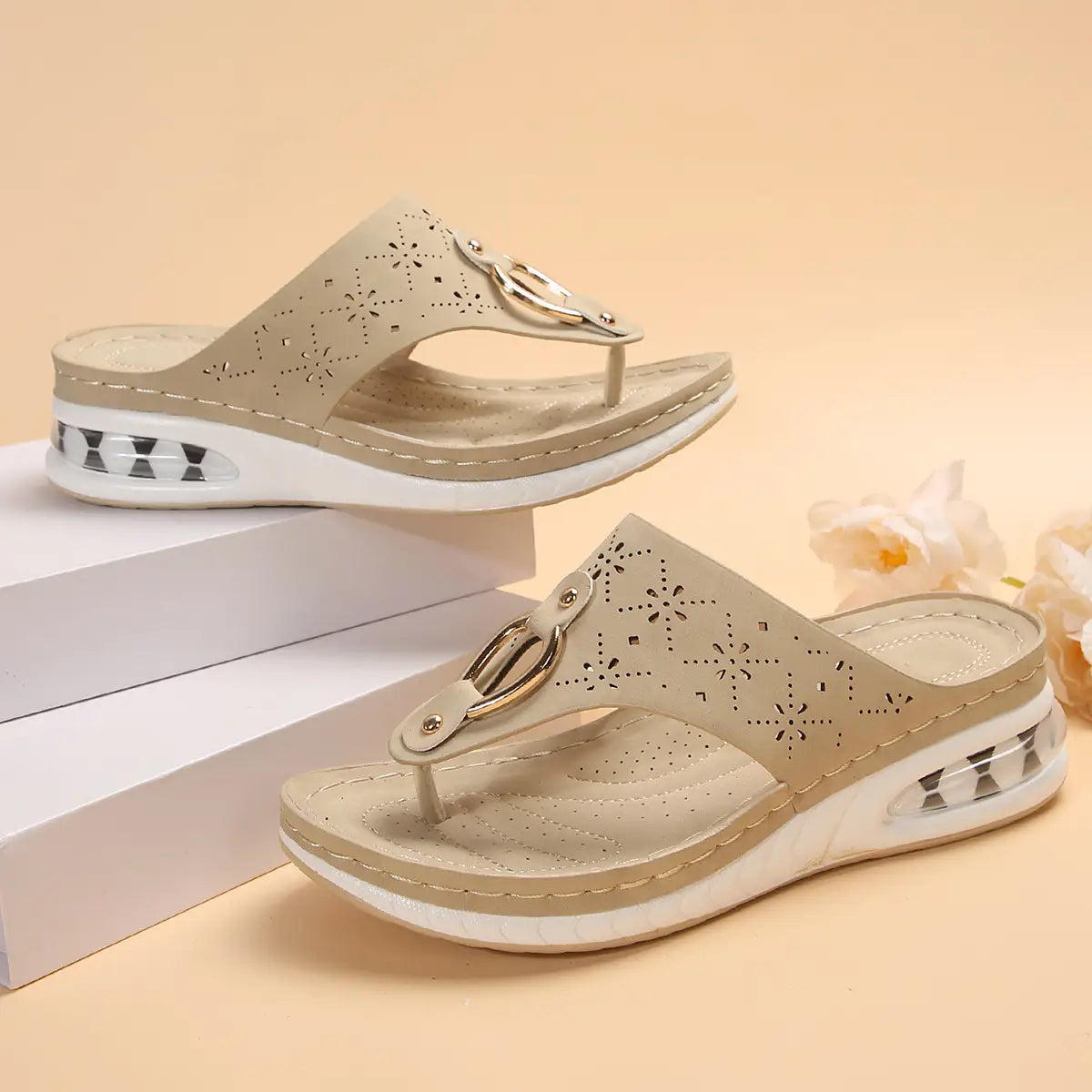 Beige leather wedge air cushion thong sandals featuring floral perforated detailing and a gold-tone buckle.