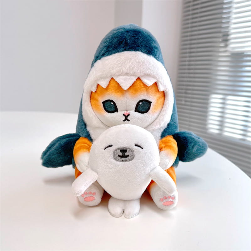 かわいらしいぬいぐるみ猫のキーホルダー。ティール色と白のサメのフーディーを着用し、小さな白いアザラシのぬいぐるみを抱えています。日本の猫の人形（だるま）風のペンダント。